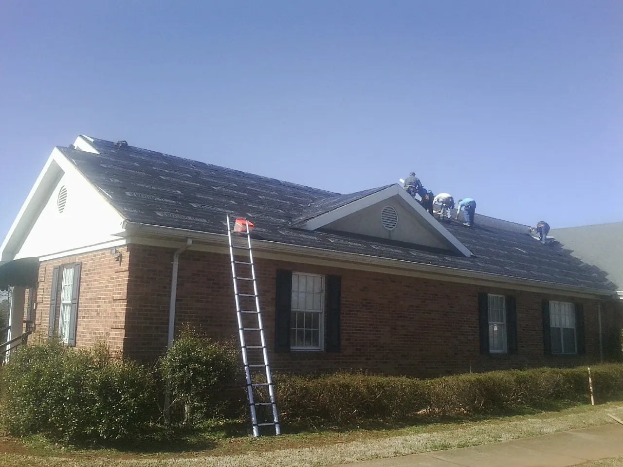 Crew tearing shingles off a brick ranch roof with a ladder set — Metal Roof Repair work by our crew in Cold Spring