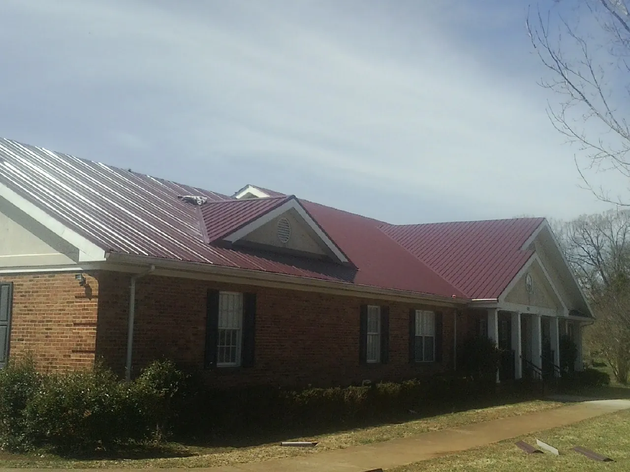 Red metal roof with gabled entries on a long brick building, from a Hail Damage Roof Repair job in Cold Spring